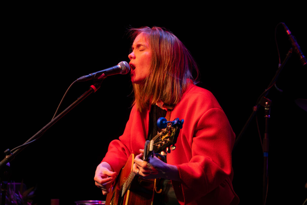 Close up on Emily Haavik singing into the microphone while playing her acoustic guitar